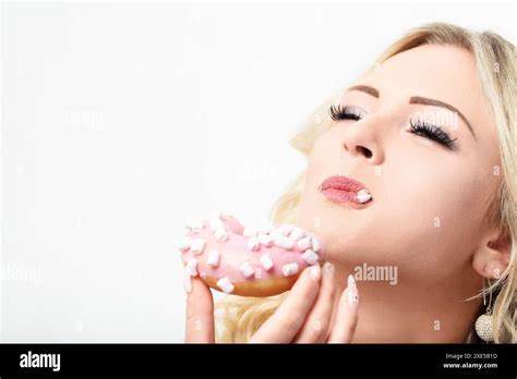 Blonde Woman Enjoys A Pink Frosted Donut With Marshmallows Indulging In Its Sweet And Tempting
