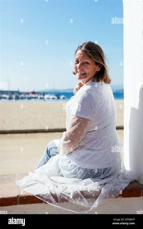 Corps complet de la femme mature positive dans des vêtements décontractés assis à la frontière