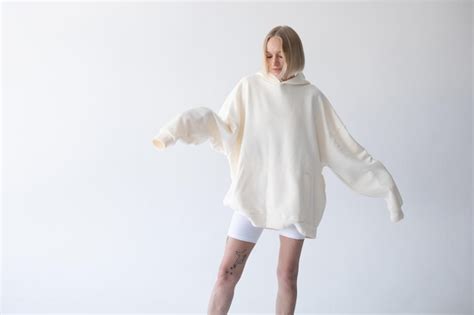 Une belle femme blonde posant dans un sweat à capuche blanc et des leggings posant sur un fond