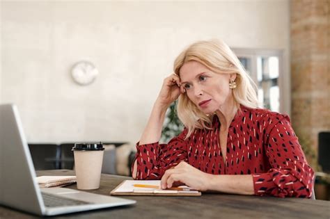 Premium Photo Serious Mature Blond Businesswoman Sitting In Front Of Laptop And Looking At