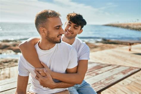 Jovem Casal Gay Sorrindo Feliz Sentado No Banco No Palco Da Praia Foto De Stock Imagem De
