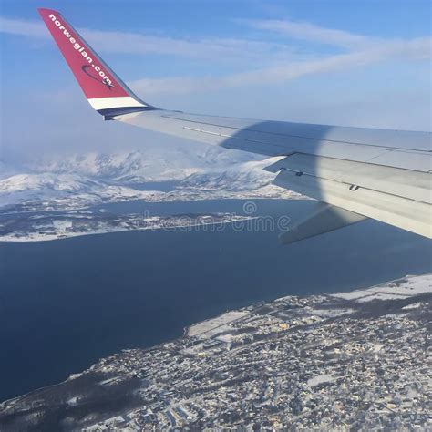 A Norwegian Plane Flying Over The Snow Covered City Of Tromso In The