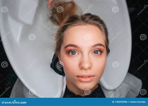 Portret Van Zitting Van De Blonde De Mooie Jonge Vrouw Op De Witte Gootsteen Van De Haarwas En