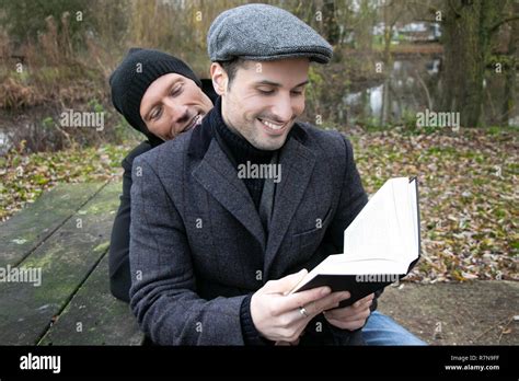 Male Gay Husbands Sit On Park Bench To Read To Each Other From Book Stock Photo Alamy