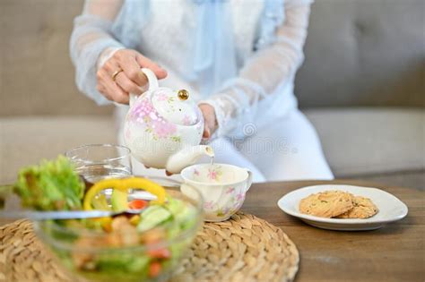 Charming Asian Aged Woman Pouring Hot Tea From Beautiful Vintage Teapot Into A Cup Stock Photo