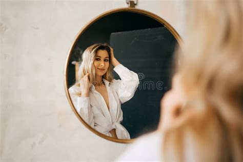 A Beautiful Blonde In A White Shirt Looks At Her Reflection In A Round