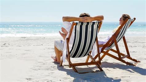 Relaxing Couple On Beach Chairs Sitting In The Sun Facing The Tropical