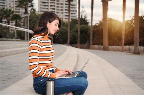 Mujer joven latina sentada al aire libre en las escaleras con una computadora portátil y