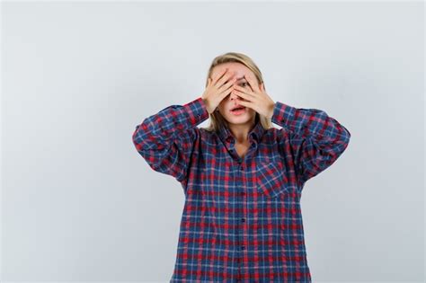 Femme blonde couvrant une partie du visage avec les mains et regardant à travers les doigts en