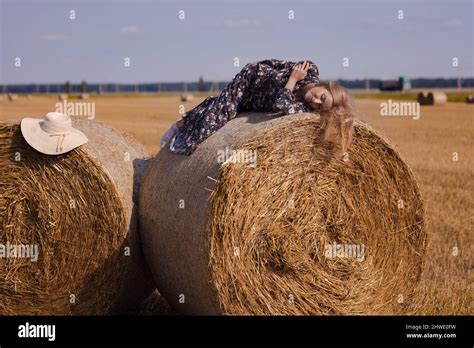 Une jeune fille blonde aux cheveux longs dans un chapeau blanc se repose et pose près des gerbes