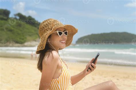 joven mujer hermosa en bikini escuchando música y usando un smartphone en la playa verano