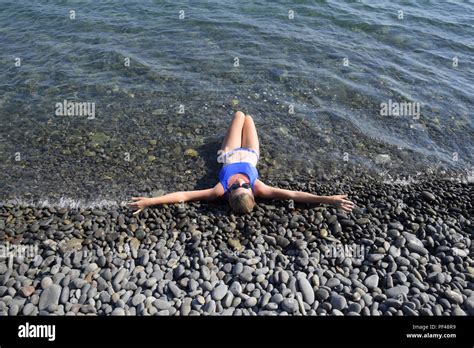 Ein schönes Mädchen in einem blauen Bikini liegt halb im Wasser am Strand Felsigen Strand