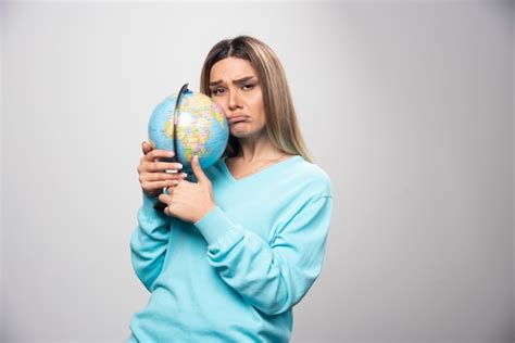 Fille Blonde En Sweat Shirt Bleu Tient Un Globe Et Semble Incertain Et Confus Photo Gratuite