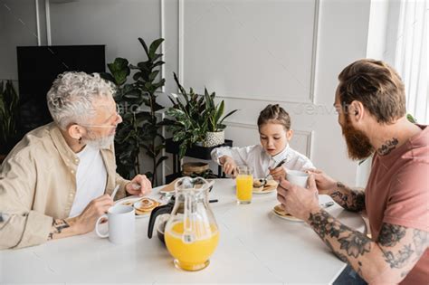 Tattooed Gay Parents Looking At Preteen Daughter Having Breakfast At Home Stock Photo By