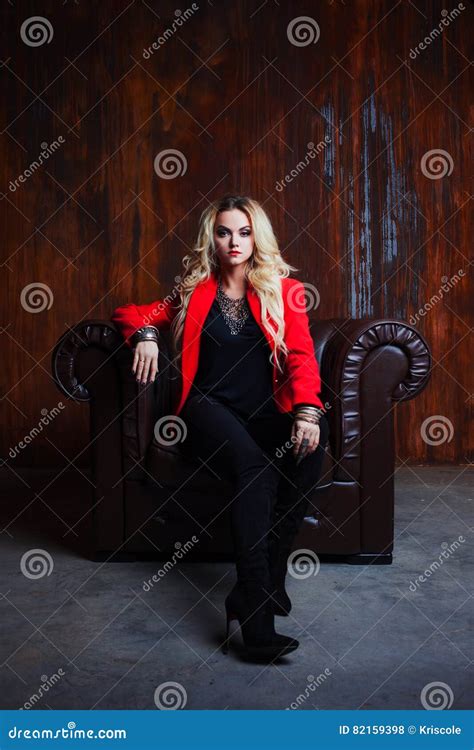 Junge Und Attraktive Blonde Frau In Der Roten Jacke Sitzt Im Ledersessel Rostige Wand Des