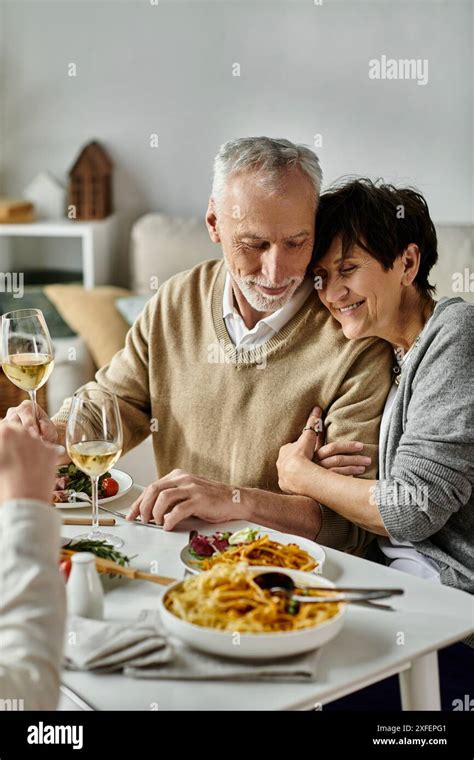Mature Parents Share Meal With Their Son And His Partner At A Cozy Dinner At Home Stock Photo