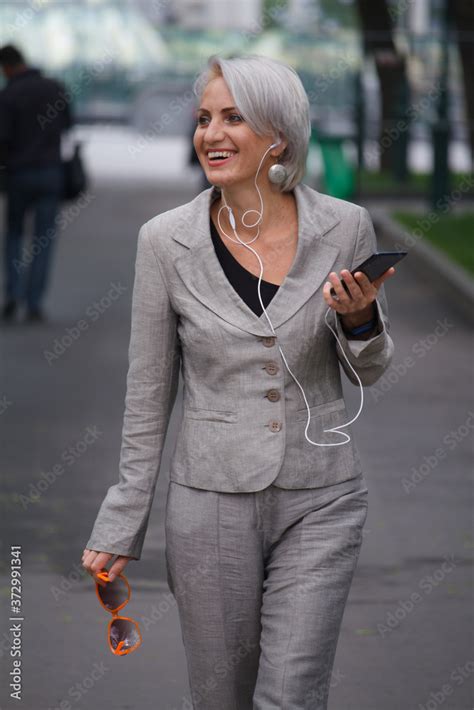 Mature Blonde Woman Walks In Public Park Listens To Music With Headphones And Smiles Selective