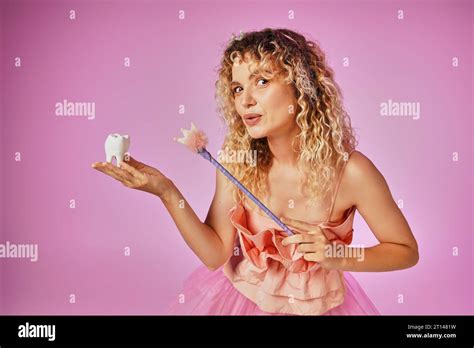 Lovely Blonde Woman In Tooth Fairy Costume Playfully Casting Spell On Baby Tooth With Her Magic