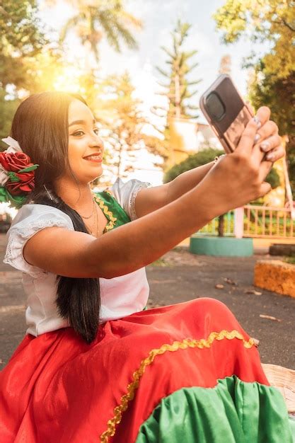 Hermosa adolescente latina con traje tradicional tomando un selfie en un parque durante un día