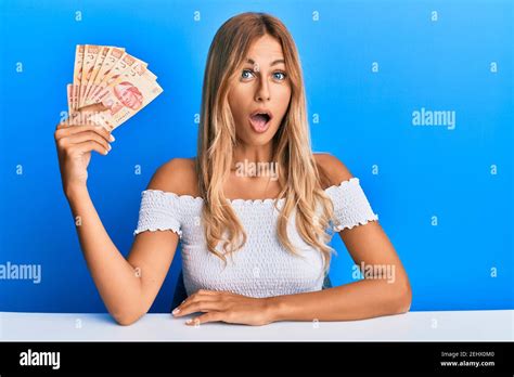 Belle jeune femme blonde détenant 100 pesos mexicains de billets effrayés et étonnés par la