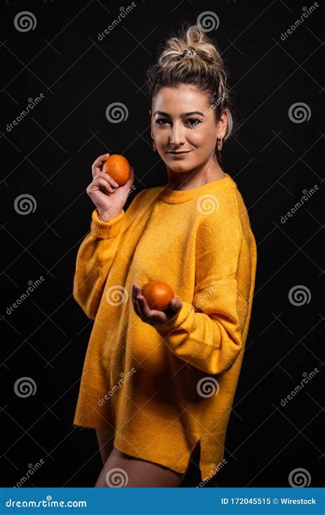 Vertical Shot Of A Blonde Girl In An Orange Sweater Posing With Clementine Fruits Stock Image