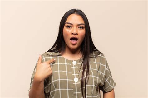 Joven mujer latina mirando consternado y sorprendido con la boca abierta apuntando a sí mismo