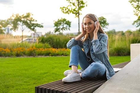 Premium Photo A Blonde Woman Sits On A Bench With Crossed Legs Enjoying Through Her Headphones