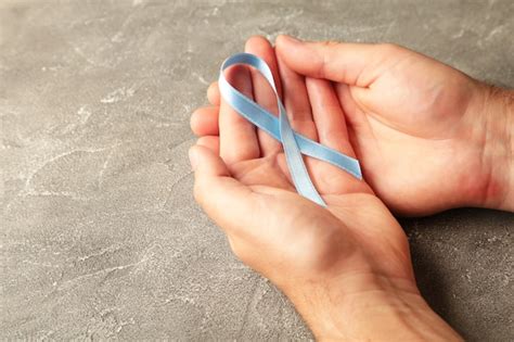 Mano que sostiene la cinta azul del cáncer de mama en la superficie