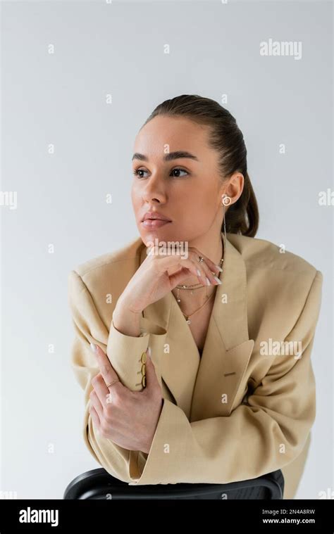 Brunette Young Woman In Beige Jacket Leaning On Chair Back While Posing