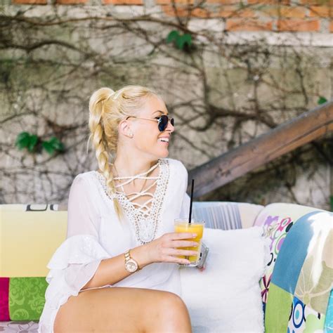 Souriante Blonde Jeune Femme Assise Sur Un Canapé Tenant Un Verre De Jus à La Recherche De Suite