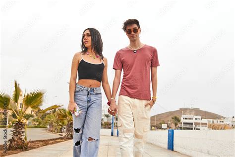 Hombre joven gay con lentes de sol camina junto de la mano a su novia quien observa más detalles