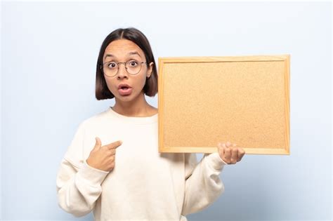 Joven mujer latina mirando consternado y sorprendido con la boca abierta apuntando a sí mismo