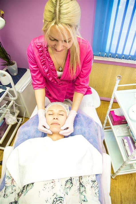 A Blonde Esthetician Wearing Gloves Performs A Facial Massage On A Client Lying On A Treatment