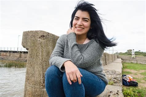Tímida joven latina sonriendo y mirando a la cámara sentada junto al río Foto Premium