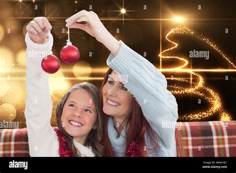 Mother And Daughter Holding Baubles Against Christmas Light Design