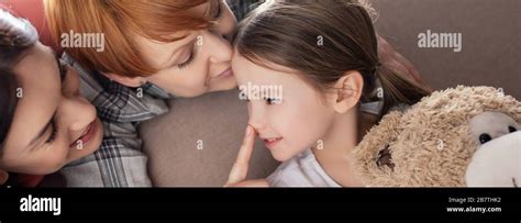 Panoramic Shot Of Smiling Same Sex Parents Kissing And Touching Nose Of Daughter With Teddy Bear