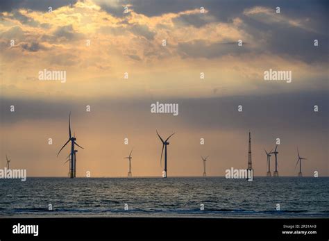 Fans Of Wind Turbines Spin Over The Sparkling Sea Dynamic Clouds At Sunset An Offshore Wind