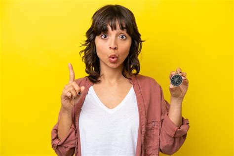 Joven latina sosteniendo una brújula aislada en un fondo amarillo con la intención de darse