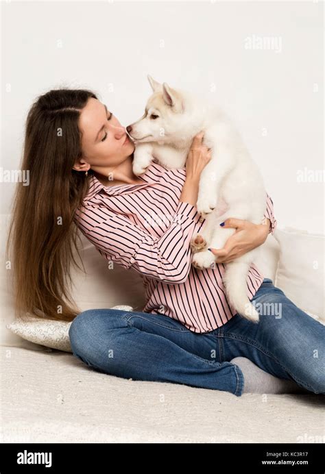 Happy Beautiful Woman Hugging Puppy Husky Girl Sitting On A Sofa And