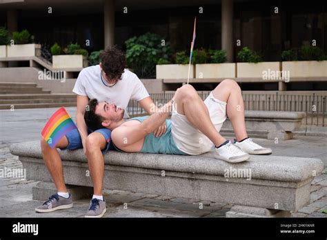 Gay Couple Laughing And Hugging Sitting On A Bench Holding LGBT Flags Stock Photo Alamy