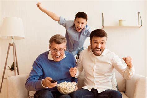 Excited Elderly Man Mature Son And Grandson Watching Sports Indoor
