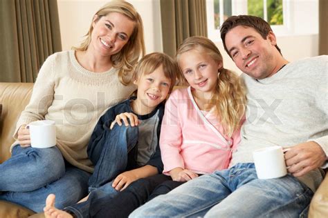 glückliche junge Familie sitzt auf Sofa holding Tassen Stock Bild