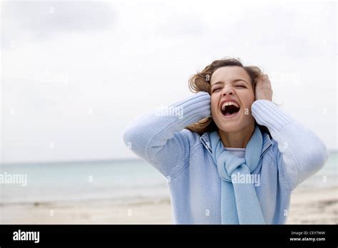 Female Long Blonde Hair Wearing Pale Blue Zip Up Jumper And Matching Scarf Standing On Beach Sea