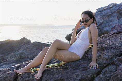 retrato de hermosa mujer de moda en bikini blanco posando en la playa de roca joven asiática