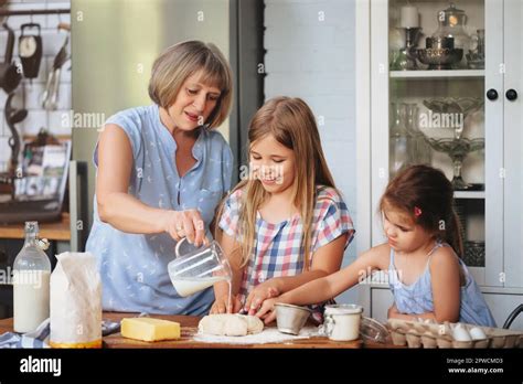 Happy Adult And Mature Women Cooking Together With Cute Girls At Table In Kitchen Stock Photo