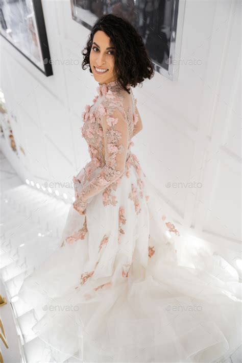 Brunette Middle Eastern Woman With Wavy Hair Standing In Gorgeous And Floral Wedding Dress Stock