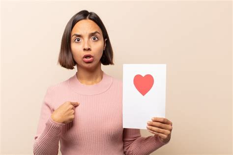 Joven mujer latina mirando consternado y sorprendido con la boca abierta apuntando a sí mismo