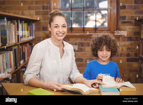 Blonde Teacher And Pupil Reading Books In The Library Stock Photo Alamy