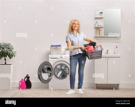 Full Length Portrait Of A Mature Woman Holding A Laundry Basket With Clothes In A Bathroom Stock