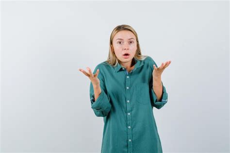 Femme Blonde Levant Les Mains Ouvrant La Bouche En Chemise Verte Et Semblant Anxieuse Photo
